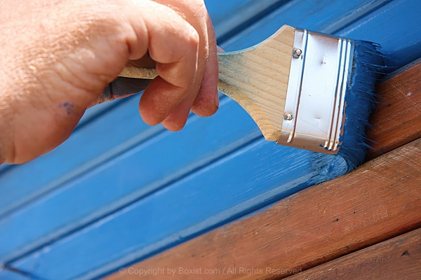 Person Using Wide Brush To Apply Blue Paint On Wooden Planks