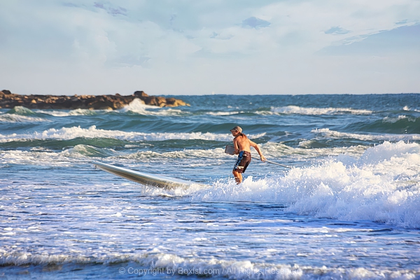 Man Surfing Waves On Stand Up Paddle Board Near Shore