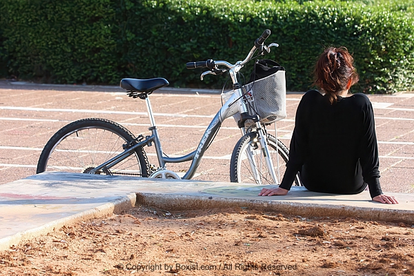 Young Woman Taking A Break On Sidewalk With Bicycle Resting Beside Her