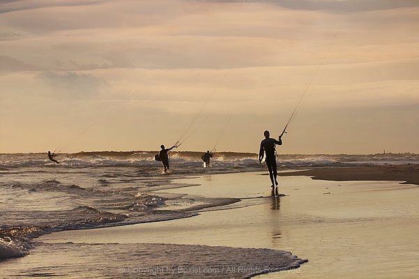 Group Of Kite Surfers Walking Along The Beach