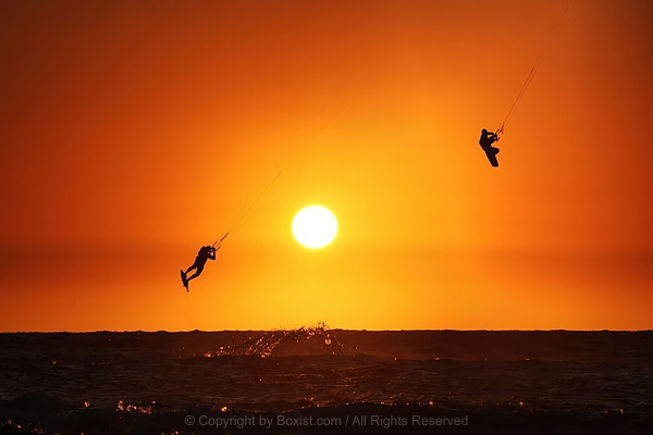 Silhouette Of Two Kite Surfers Flying Over Sea At Sunset