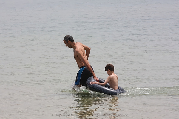 Man Dragging Boy In Rubber Tire Through Sea Water Father And Son Fun
