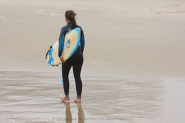 Young Woman Carrying Surfboard Along Sandy Shore