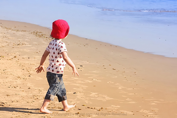 Little Boy Walking On Sandy Beach Approaching Water
