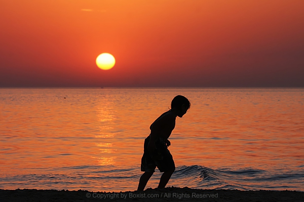 Silhouetted Child Plays On Shoreline As Sunset Glows