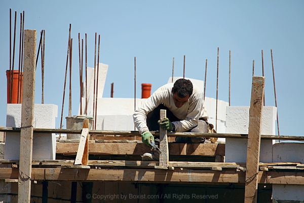 Construction Worker Kneels To Hammer Wood On Building Frame