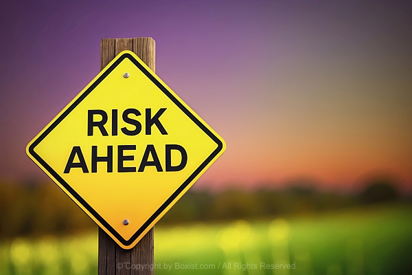 Yellow Risk Ahead Warning Sign On Wooden Pole Against Blurry Landscape