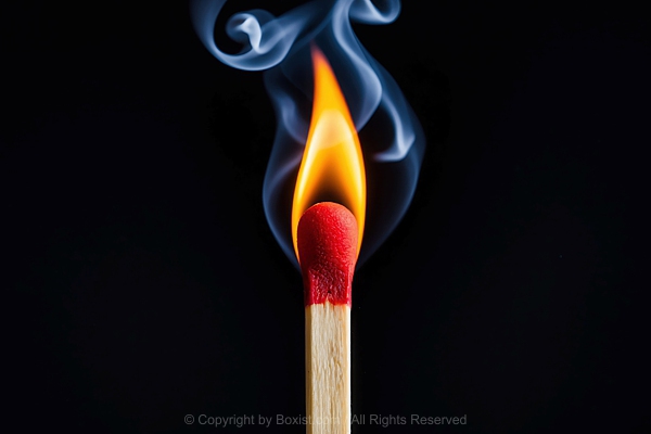 Closeup Of Lit Matchstick With Wisps Of Smoke Against Black Background